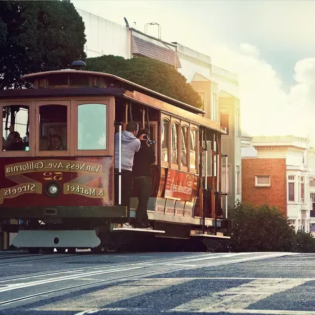 Un tram costeggia una collina a San Francisco, mentre i passeggeri guardano fuori dal finestrino.