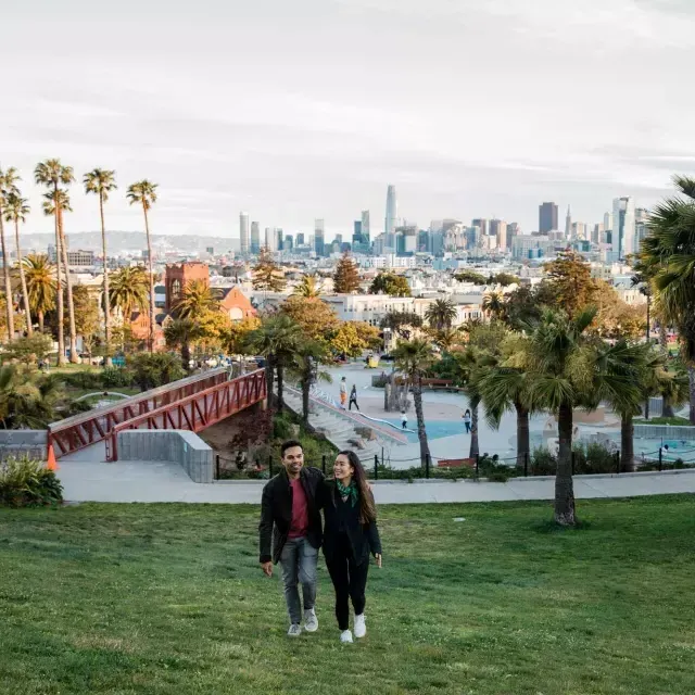 Ein Paar geht auf die Kamera zu, im Hintergrund Dolores Park und die Skyline von San Francisco.